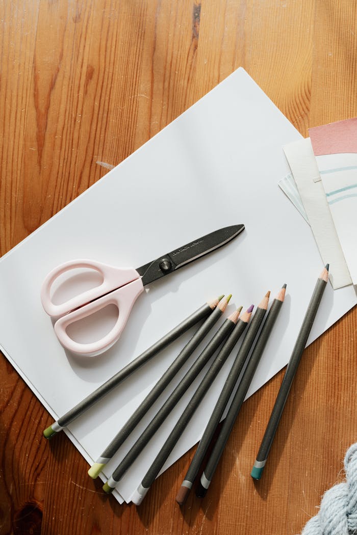 about-bg A collection of colored pencils, scissors, and paper on a wooden table, ideal for artistic projects.