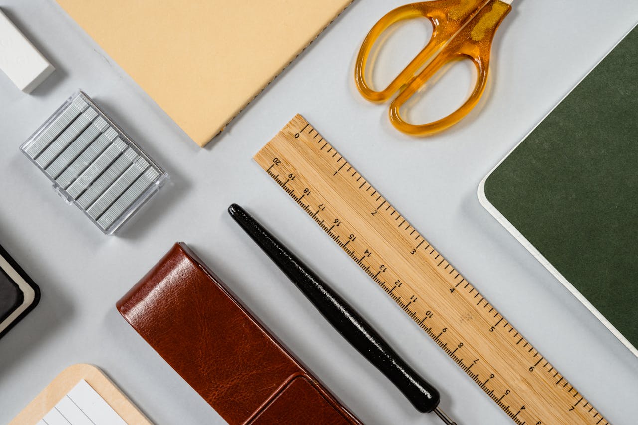 A neatly arranged flat lay of office supplies including scissors, ruler, fountain pen, and notebooks.